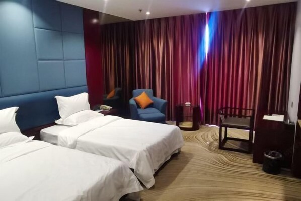 Ein Hotelzimmer mit zwei Betten, einem blauen Sessel, einem kleinen Tisch und einem Schreibtisch.