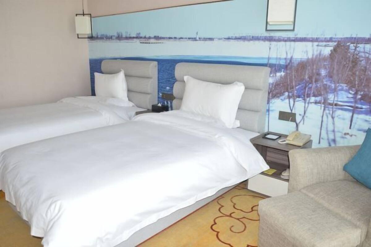 Habitación de hotel con dos camas, un sofá, una mesita de noche con teléfono y un mural en la pared que representa un paisaje invernal.