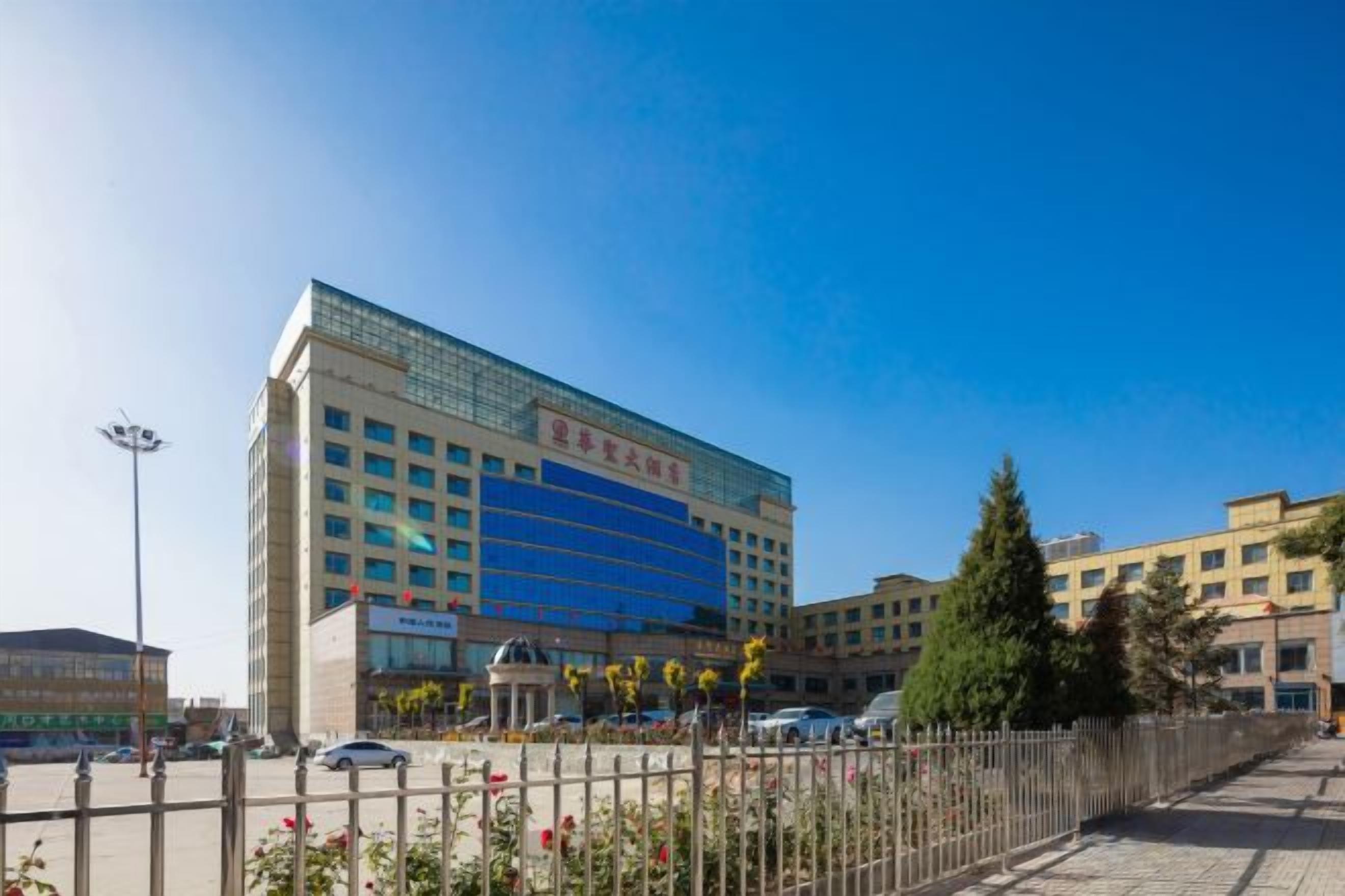 A multi-story hotel with a modern facade, a parking lot, and a fenced garden area.