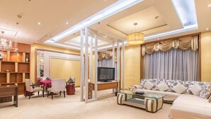 A modern living room with a sofa, coffee table, TV, and a dining area with chairs and a table. - Huasheng Hotel (Shanyin)