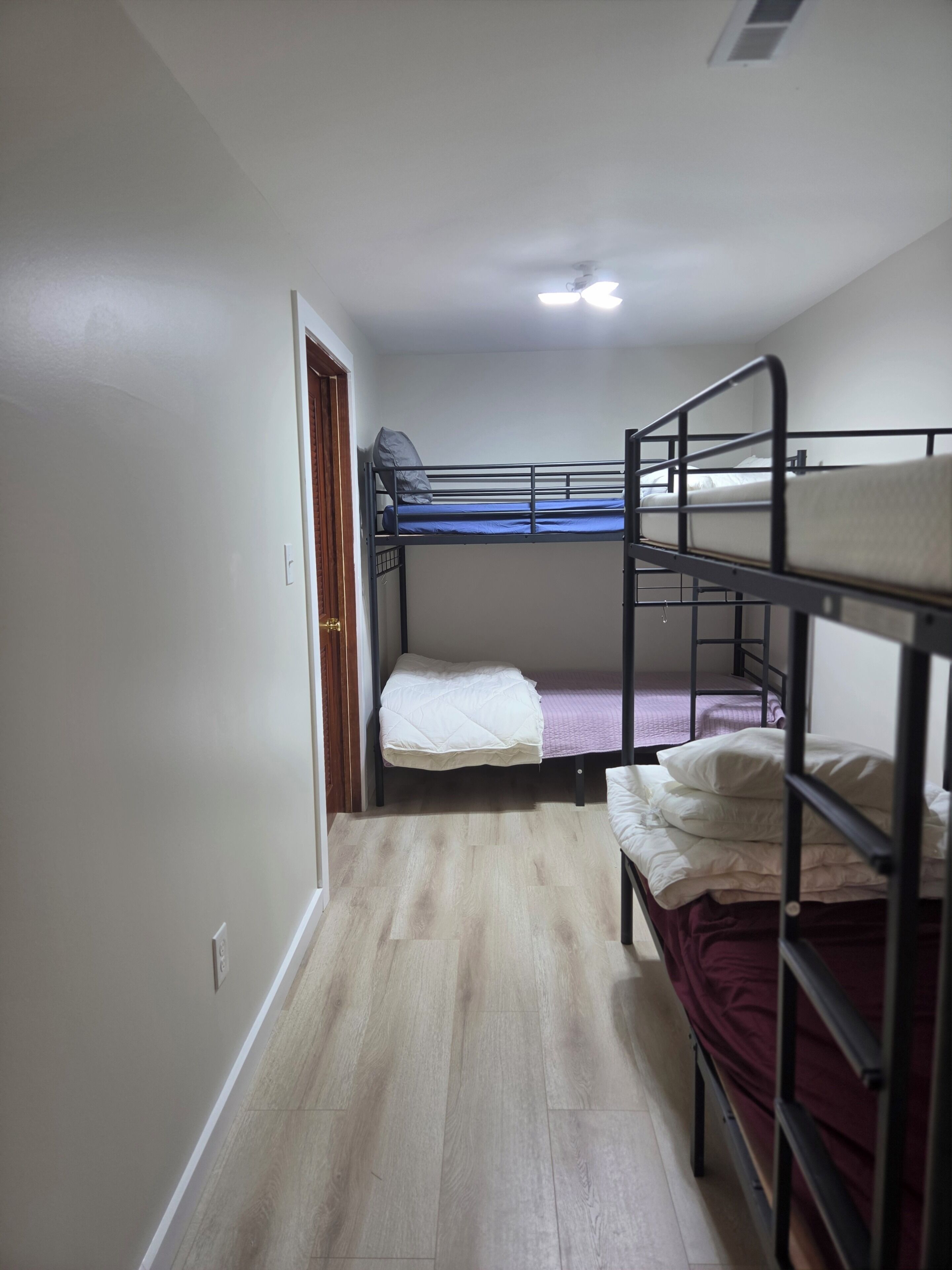 Una habitació de dormitori amb lliteres, una porta de fusta i un terra de fusta de color clar.
