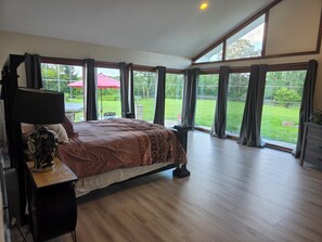 A bedroom with a large bed, a desk with a lamp, and a view of a green garden through large windows. - Charming 4-bedroomHorse Ranch farmhouse in enjoyable Lebanon with AC, Wifi (Lebanon)