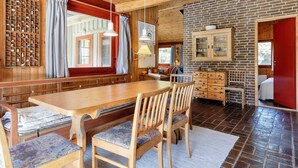 A wooden interior with a long dining table, chairs, a brick wall, and a red door. - 6 Person Holiday Home in Blokhus (Blokhus)