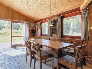 A wooden interior with a large table and chairs, large windows with curtains, and a view of greenery outside. - 6 Person Holiday Home in Blokhus (Blokhus)