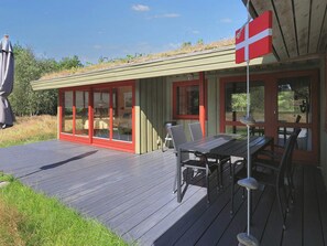 En modern uteplats med ett matbord och stolar, en flagga och en byggnad med stora glasdörrar.