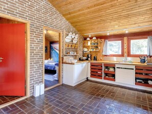 A compact kitchen with a brick wall, wooden ceiling, and a red door. - 6 Person Holiday Home in Blokhus (Blokhus)