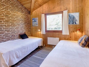 A room with two beds, a window with curtains, a radiator, and a painting on the wall. - 6 Person Holiday Home in Blokhus (Blokhus)