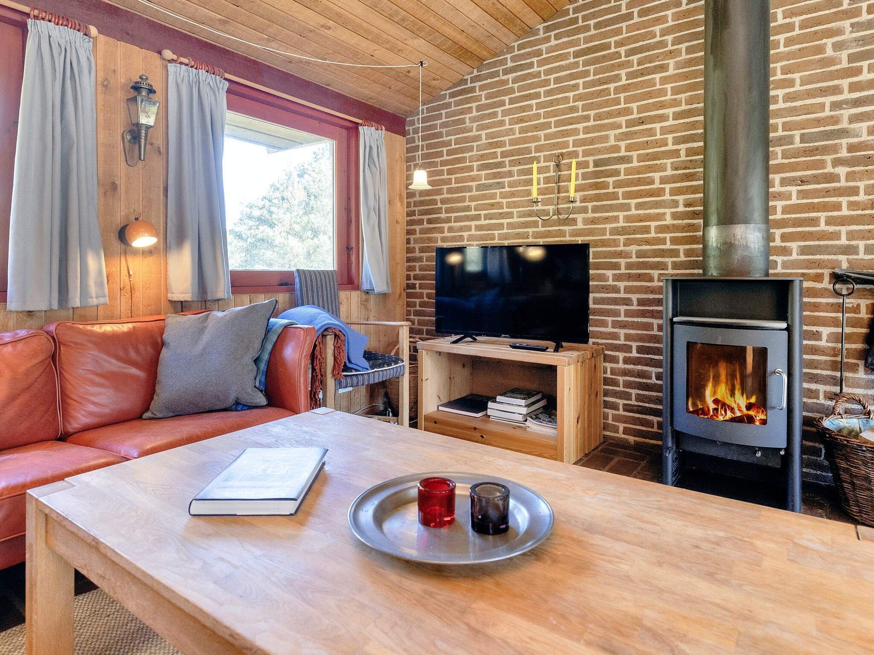 Ein gemütliches Wohnzimmer mit Ledersofa, Couchtisch aus Holz, Flachbildfernseher und Kaminofen.