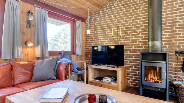 A cozy living room with a leather sofa, a wooden coffee table, a flat-screen TV, and a wood-burning stove. - 6 Person Holiday Home in Blokhus (Blokhus)