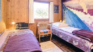 A cozy cabin room with two beds, a wooden chair, a window with curtains, and a quilted wall hanging. - 6 Person Holiday Home in Blokhus (Blokhus)