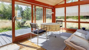 A room with a wooden floor, a round table with chairs, a sofa, and large windows with blinds. - 6 Person Holiday Home in Blokhus (Blokhus)