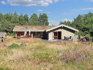 A small, single-story cabin with a red door and a covered porch, surrounded by natural vegetation. - 6 Person Holiday Home in Blokhus (Blokhus)