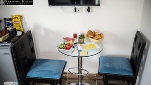 Pieni ruokailutila, jossa on pyöreä lasipöytä, kaksi sinistä, pehmustettua tuolia sekä erilaisia ruoka-aineita, kuten leipää, vihanneksia ja mausteita.