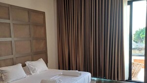 A modern hotel room with a large bed, a headboard with a geometric pattern, and a view of the outdoors through a large window with curtains. - Princi Potes Luxury Suites (Ksamil)