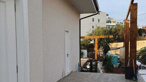 A balcony with a tiled floor, a white door, and a view of neighboring buildings and greenery. - Princi Potes Luxury Suites (Ksamil)