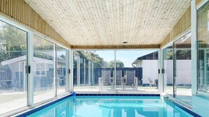 Piscina interna com teto de madeira e grandes portas de vidro que dão para o exterior.