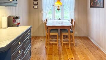 A dining area with a wooden table and chairs, a hanging light fixture, and a window with sheer curtains.