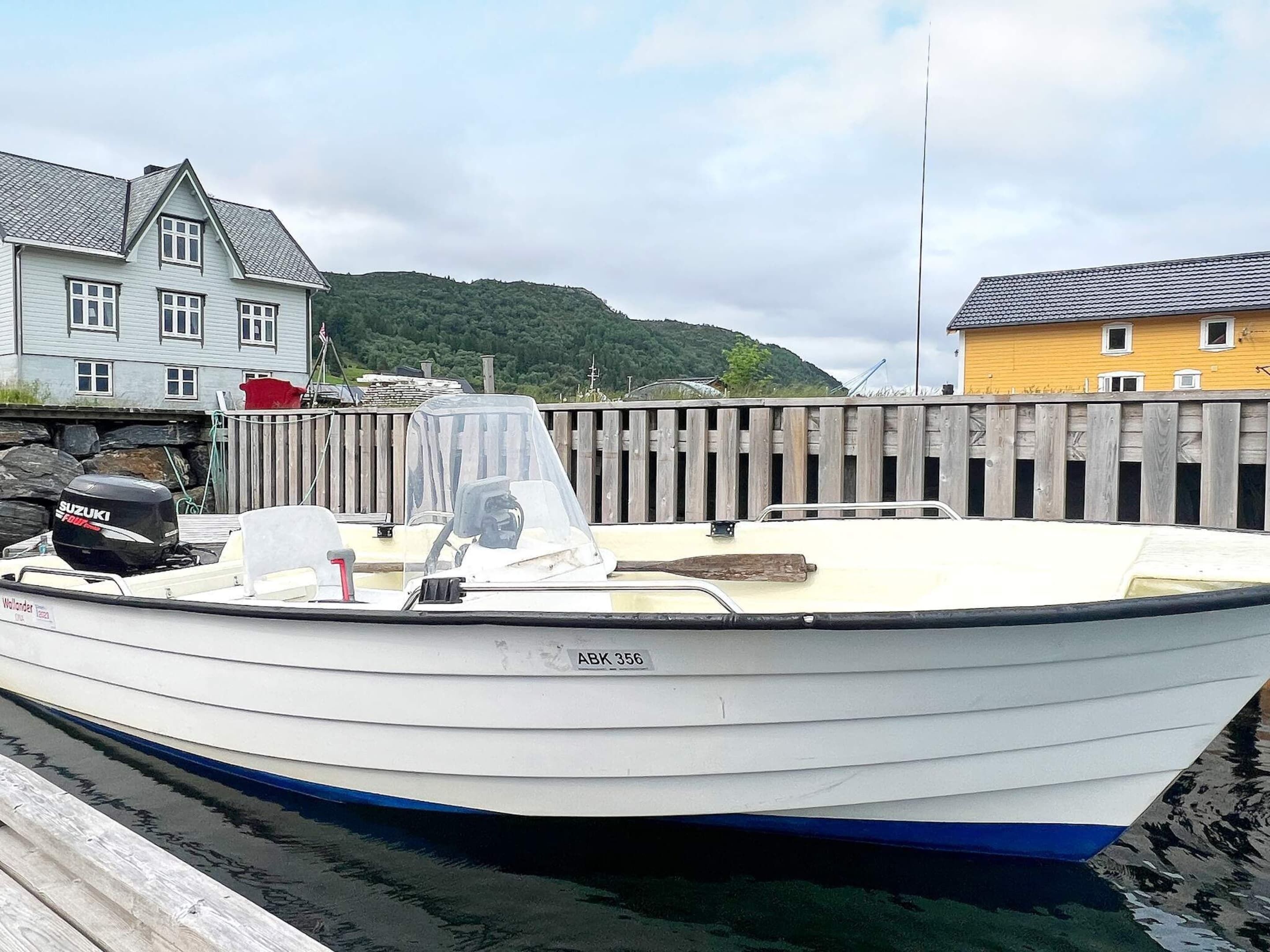 A small white boat docked at a wooden pier with a house in the background.