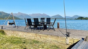 A wooden deck with a table and chairs overlooking a lake, with mountains in the background. - 7 Person Holiday Home in Gurskoy (Heroy)