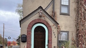 A house with a light blue door, a brick archway, and a small porch with steps. - Historic Twin Tudors Inn Southeast Room (KP1400SE) (Sioux Falls)