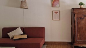 A living room with a red sofa, a wooden cabinet, and two framed artworks on the wall. - Joli Appartement à 50 Mètres de la Plage et Proche D'un Port de Pêche Typique (Saint-Pierre-d'Oléron)