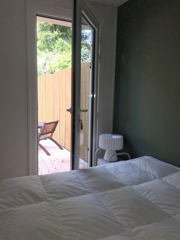 A bedroom with a bed, a chair, and a table outside a sliding glass door.