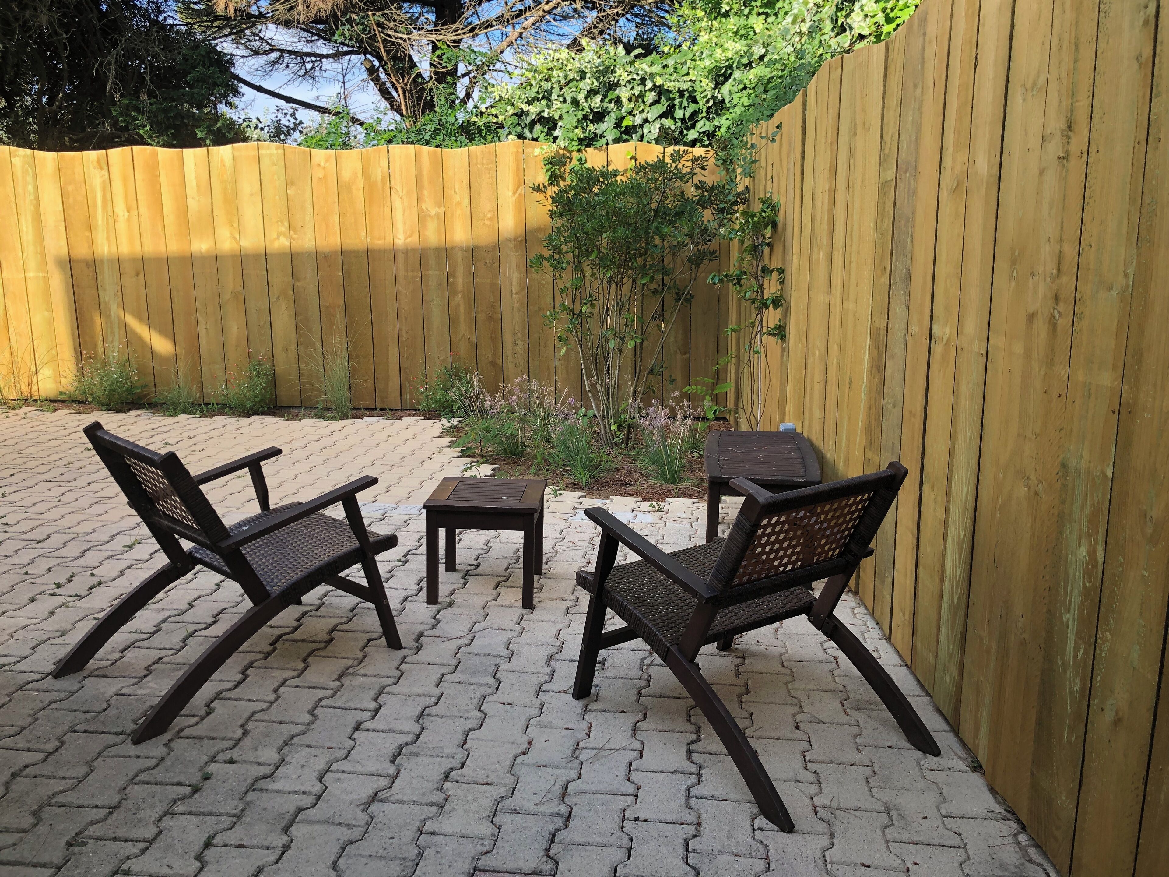 Une terrasse avec deux fauteuils en osier et une petite table, entourée d’une clôture en bois et de verdure.