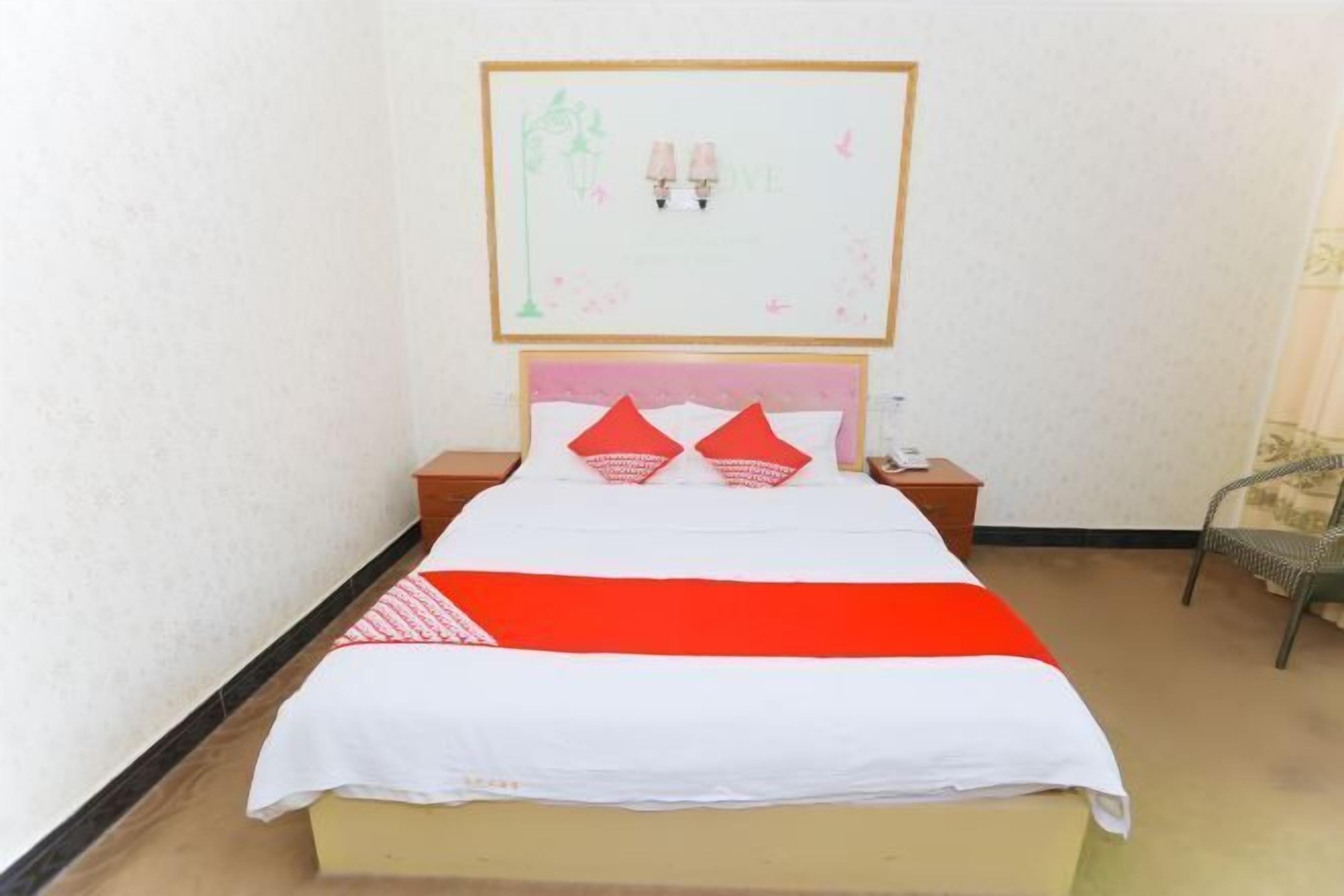 A bed with a white and red bedspread, two nightstands, a framed picture on the wall, and a chair in the corner.