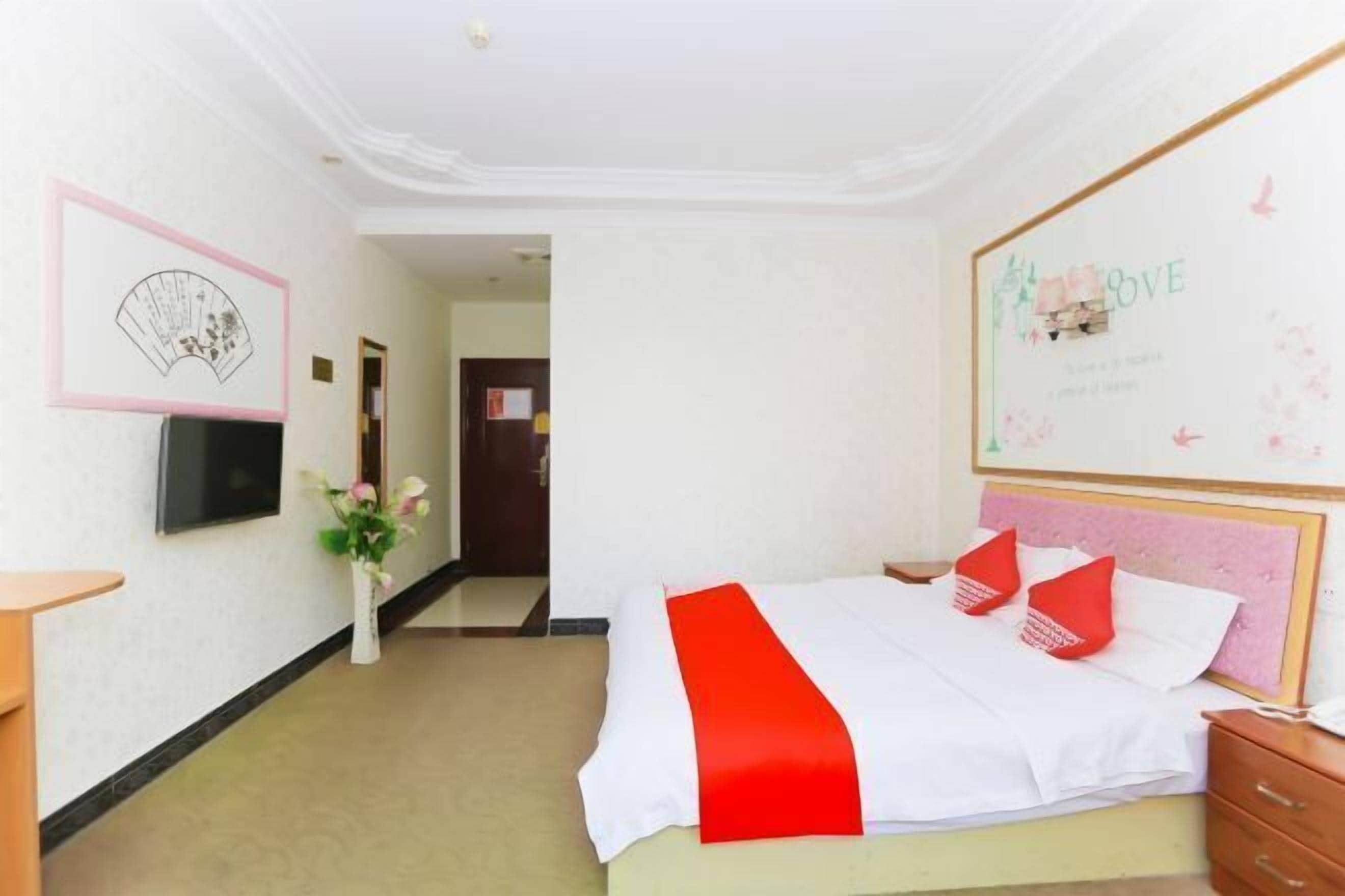 A hotel room with a bed, a bedside table, a wall-mounted TV, and a framed artwork.