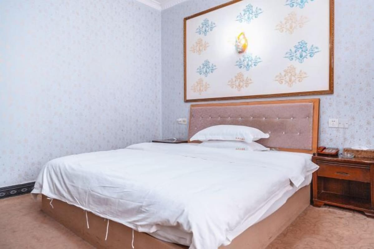 A neatly made bed with a white bedspread and pillows, a wooden nightstand with a lamp, and a wall-mounted light fixture with a floral pattern.
