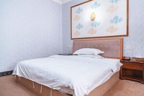 A neatly made bed with a white bedspread and pillows, a wooden nightstand with a lamp, and a wall-mounted light fixture with a floral pattern.