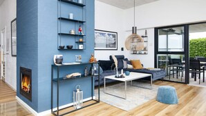 Un salon moderne avec une cheminée, des étagères bleues, un canapé et un coin repas visible à travers des portes vitrées.