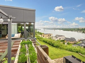 A modern house with a balcony overlooking a river, a bridge, and a marina.