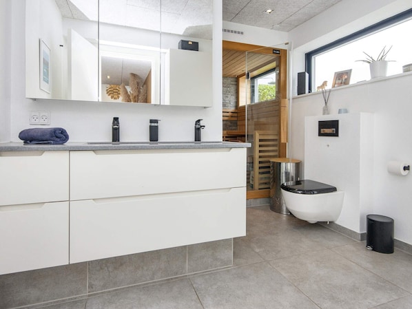 A modern bathroom with a large mirror, white cabinets, a toilet, and a sink with a towel on the counter.
