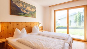 Un lit double avec une tête de lit en bois, une literie blanche et un tableau représentant un paysage de montagne au-dessus.
