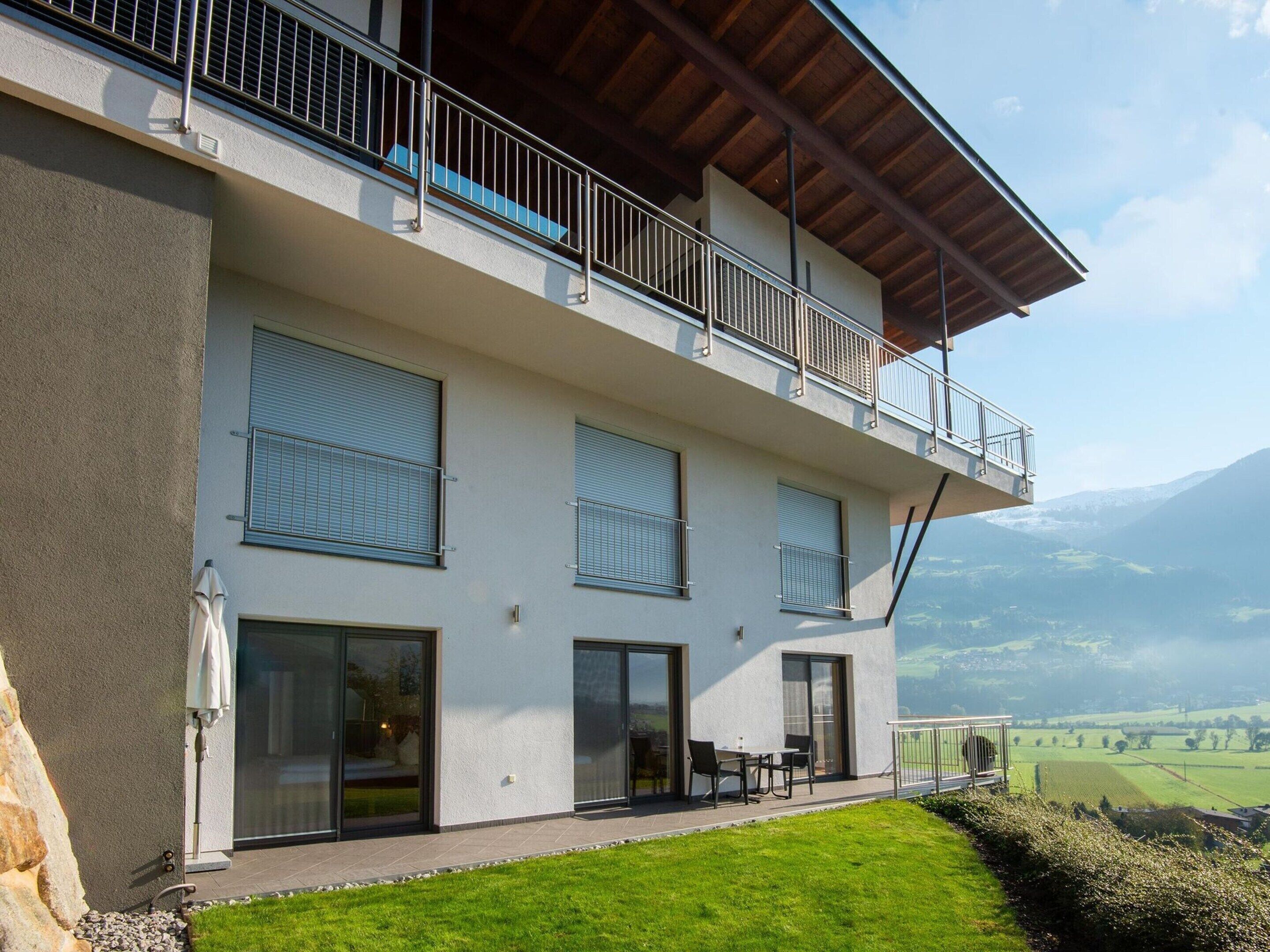 A modern two-story building with a balcony, large windows, and a view of a mountainous landscape.