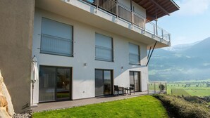 Un bâtiment moderne à deux étages, doté d’un balcon, de grandes fenêtres et offrant une vue sur un paysage montagneux.