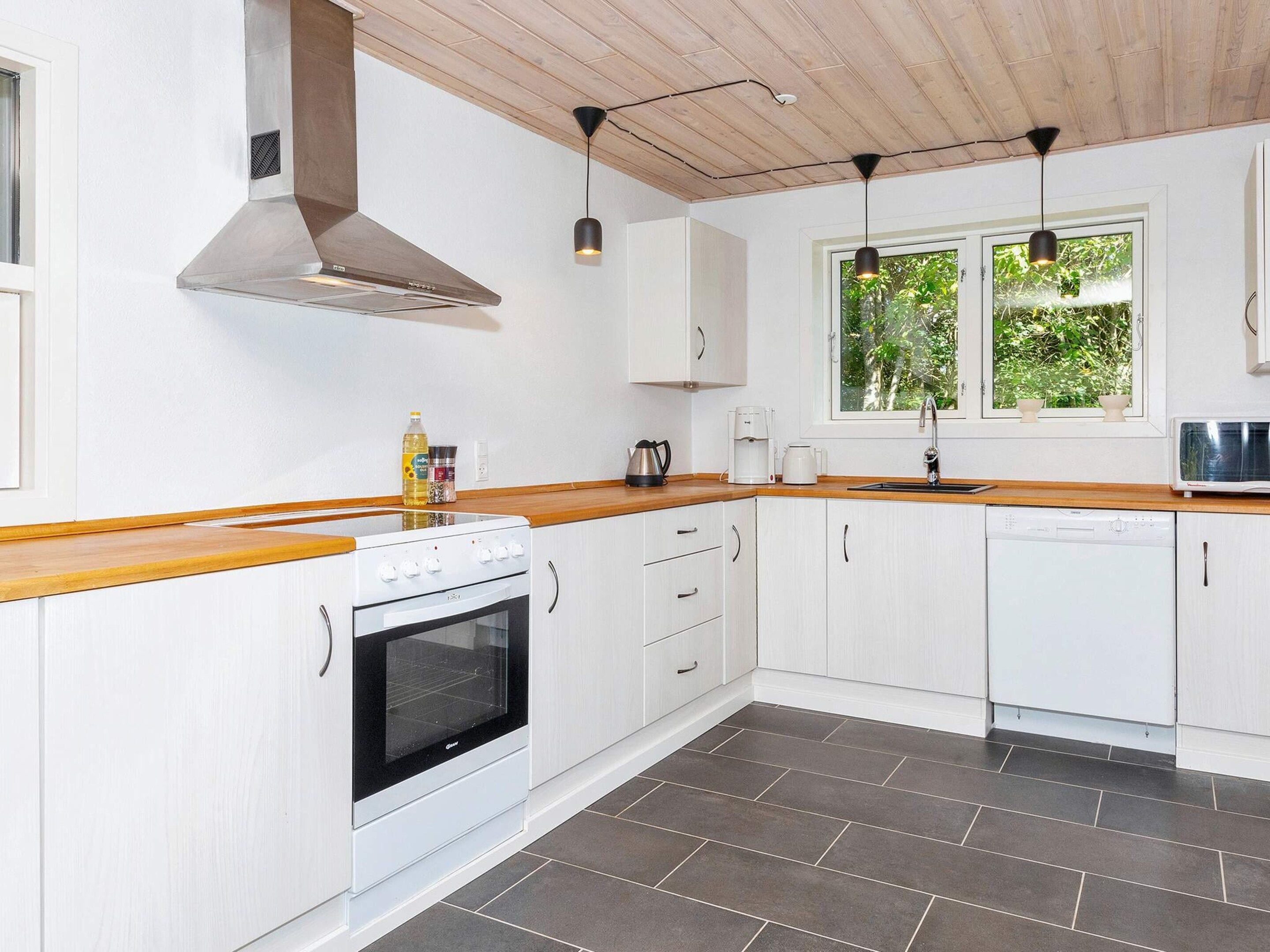 A kitchen with white cabinets, a stainless steel range hood, a built-in oven, a microwave, and a window with a view of greenery.