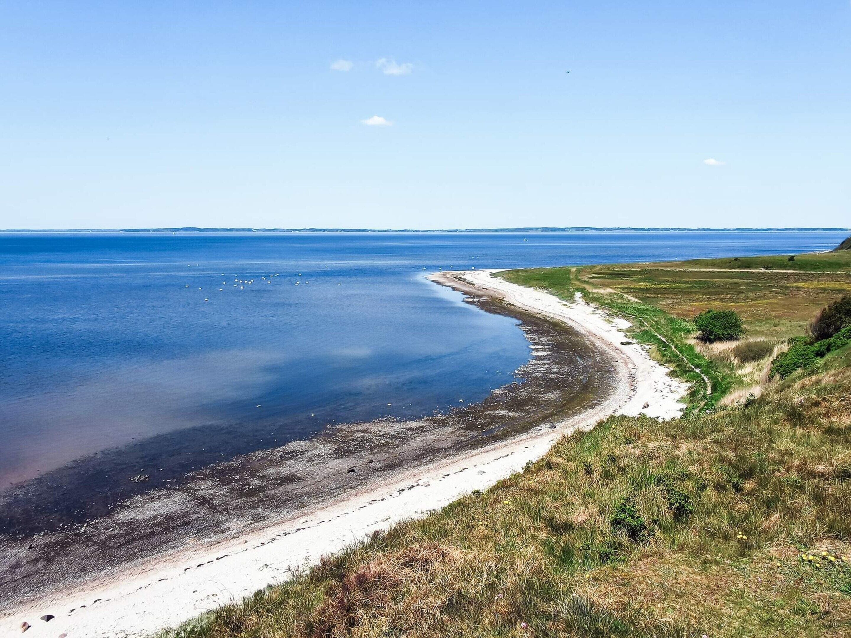 A coastal landscape with a sandy beach, grassy areas, and a clear view of the sea.