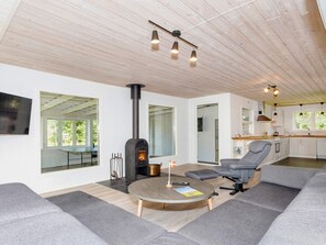 A modern living room with a wood-burning stove, a dining area, and a kitchen with white cabinets and a wooden countertop. - 4 Star Holiday Home in Gedsted (Gedsted)