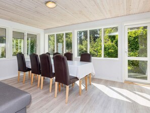 Een eethoek met een tafel, stoelen, grote ramen en uitzicht op groen.