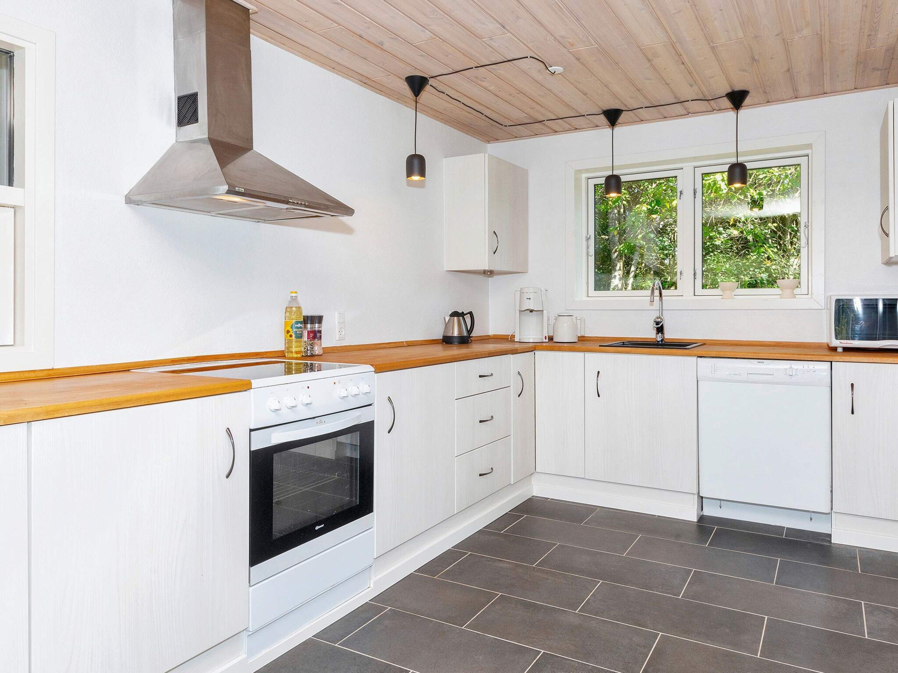 Een moderne keuken met witte kasten, een houten aanrecht, een rvs afzuigkap, een inbouwoven, een vaatwasser en een raam met uitzicht op groen.