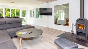A modern living room with a fireplace, a sofa, a round coffee table, and a TV mounted on the wall. - 4 Star Holiday Home in Gedsted (Gedsted)
