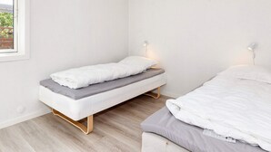A small, single-bed room with a wooden floor, white walls, and a window with a view of greenery outside. - 4 Star Holiday Home in Gedsted (Gedsted)