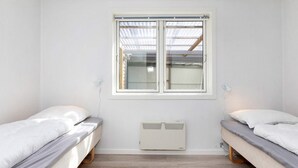 Habitació amb dos llits, una finestra i un calefactor penjat a la paret.