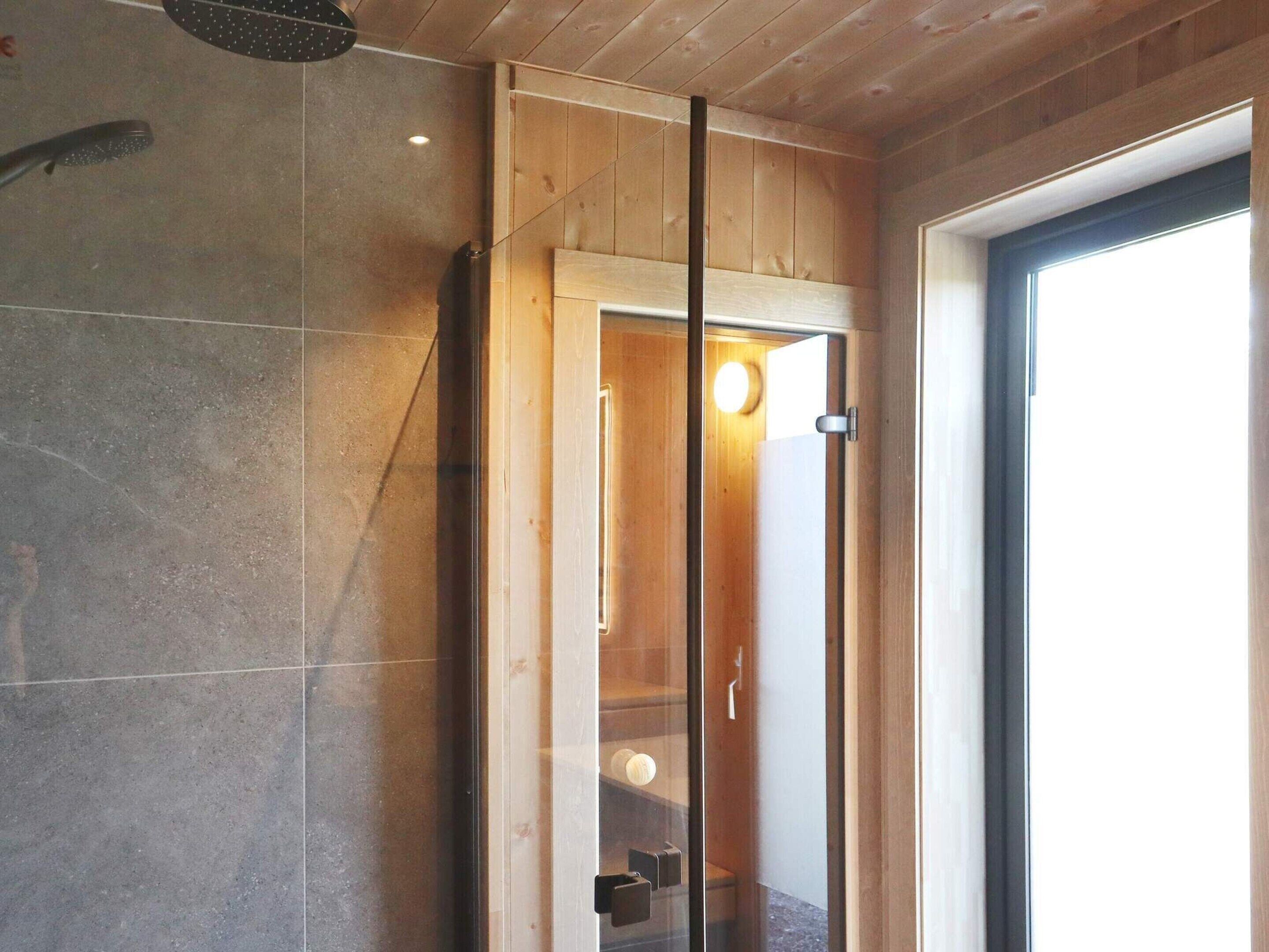 Un baño moderno con cabina de ducha de vidrio, paneles de madera y un ventanal grande.