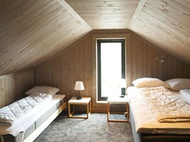 Un dormitorio acogedor y pequeño en el ático, con dos camas individuales, una ventana y una lámpara.