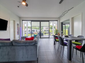Een moderne woonkamer met een grijze bank, een eettafel met stoelen en een grote glazen schuifdeur die leidt naar een terras.