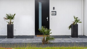 A modern building entrance with a black door, a mailbox, and two potted plants. - Villa With Covered Terrace and Jetty on the Water (Zeewolde)