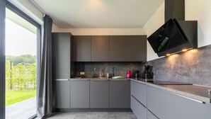 A modern kitchen with grey cabinets, a large window with curtains, and a flat-screen TV mounted above the counter. - Villa With Covered Terrace and Jetty on the Water (Zeewolde)